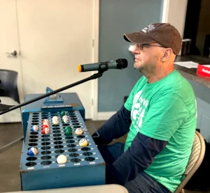 Bingo caller wearing green volunteer T-shirt and a brown cap.